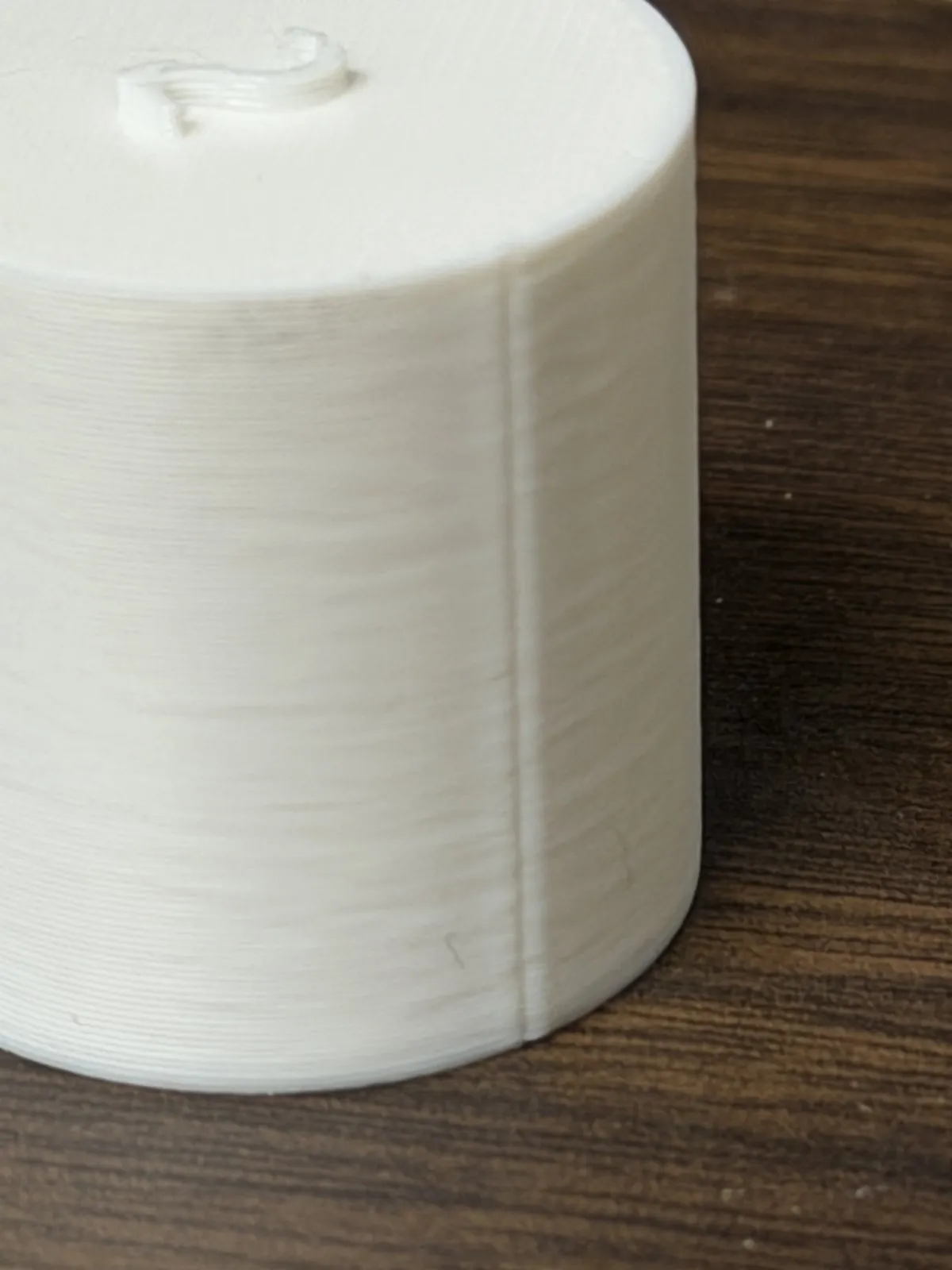 Close-up of a white PLA cylinder printed with the stock profile, with a sharp raised seam ridge running the full height of the side