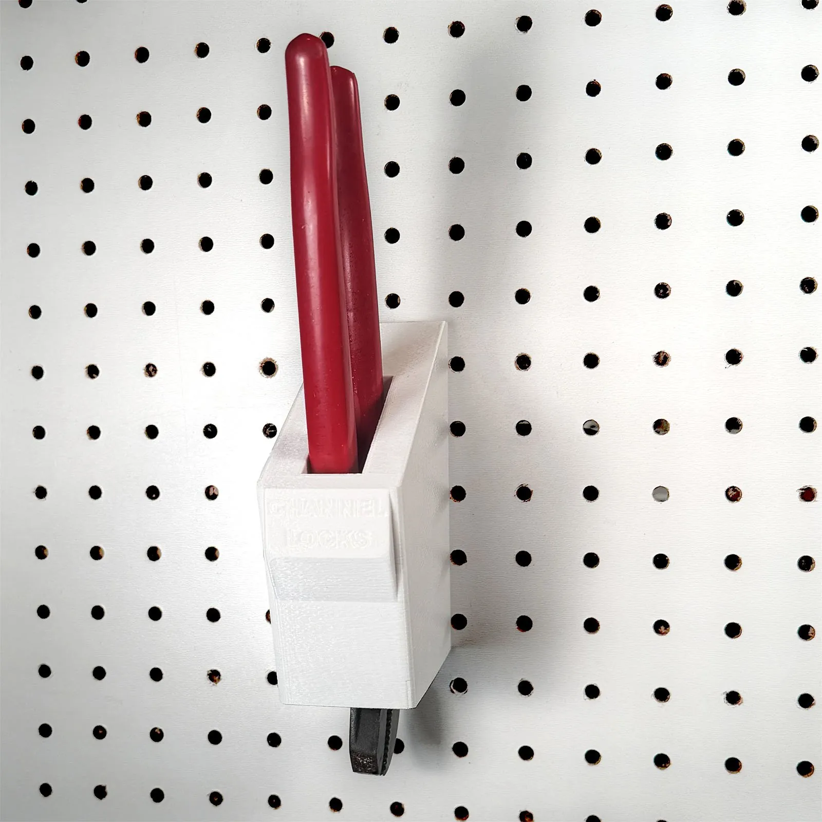 Front view of the holder on pegboard with CHANNEL LOCKS lettered on a raised tab on the front, the red handles standing up out of the slot and the tips of the jaws showing under the bottom