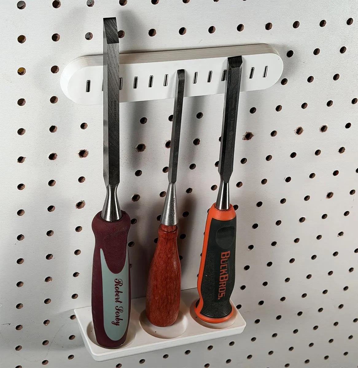 Close-up of the three chisels standing in the rack, each handle end resting in its own round countersink, with the blades leaning back against the magnets on the bar above