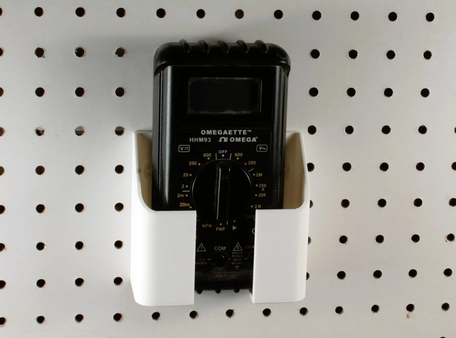 The same pegboard holder holding a black Omega HHM93 handheld multimeter