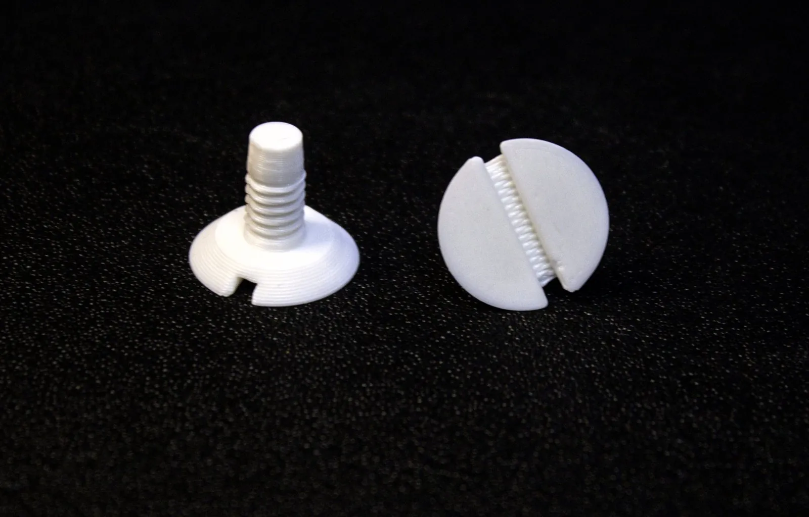Two 3D printed white slotted screws with countersunk heads, one standing on its head and one lying face up