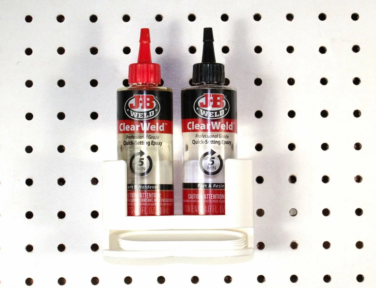 Front view of the rack on pegboard with two J-B Weld ClearWeld bottles, the Part B Hardener and Part A Resin labels showing through the open front, and the edges of the mixing trays in the slot below
