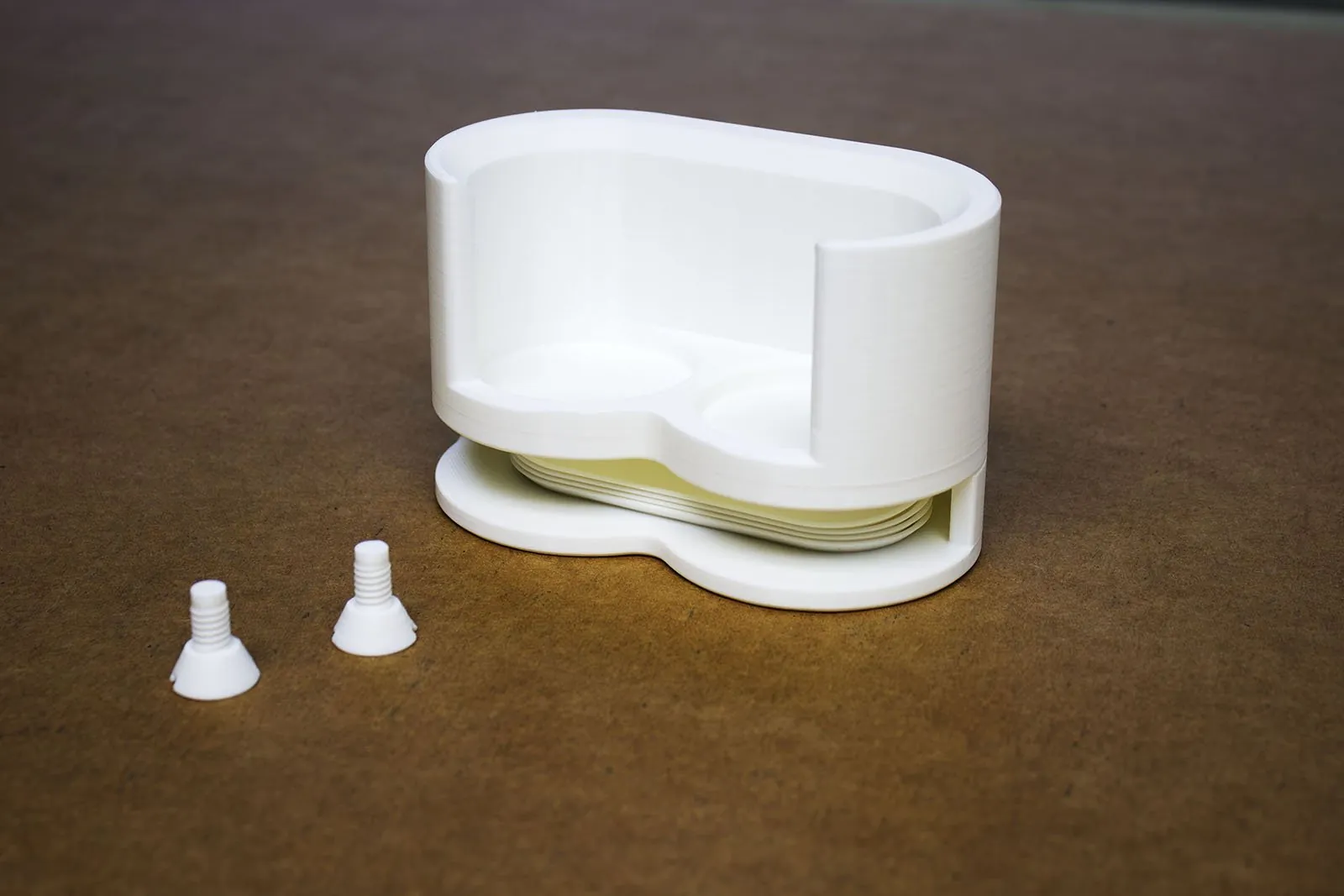 The empty rack on a brown work surface with four mixing trays stacked in the slot under the bottle pockets, and two white 3D printed screws in front of it