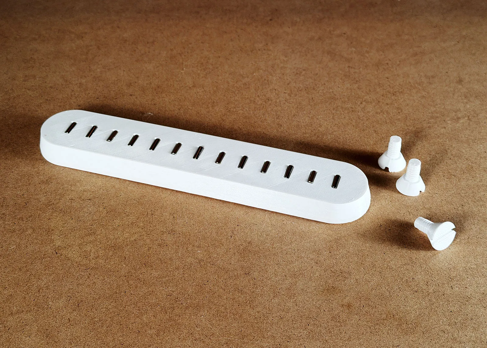 The printed bar with all 13 magnets in place lying on a brown work surface next to three white printed screws