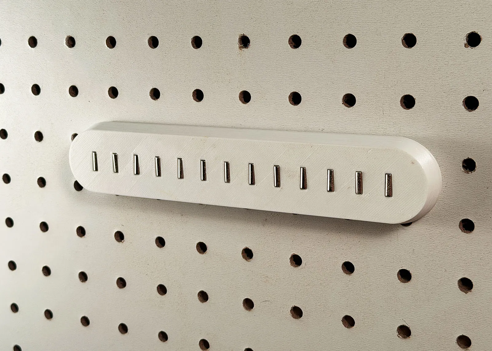 Close-up of the empty magnetic bar on pegboard, showing 13 silver cylindrical magnets sitting in slots across its front