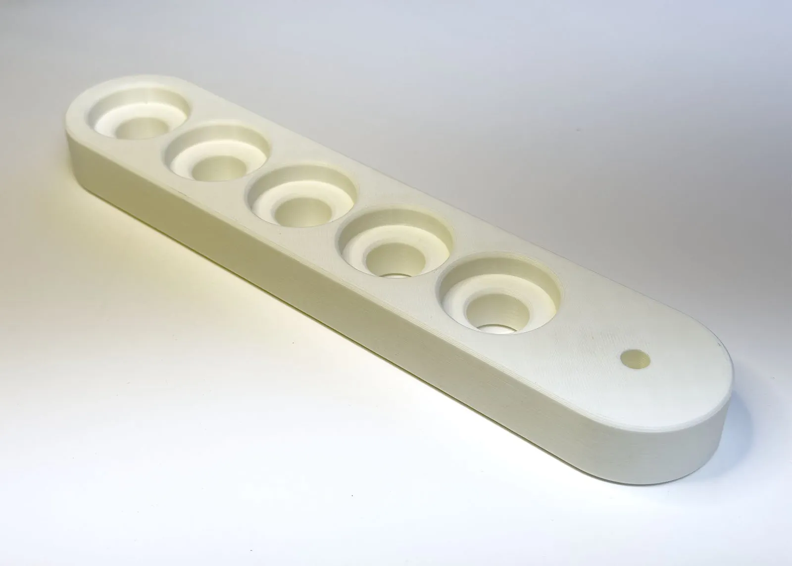 The printed arm on its own, showing five holes in a row, each with a wide shallow counterbore on top, and the small hinge pin hole at one end